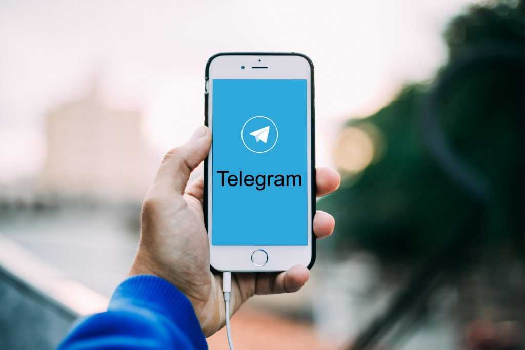 Person holding a smartphone displaying the Telegram app on the screen outdoors.